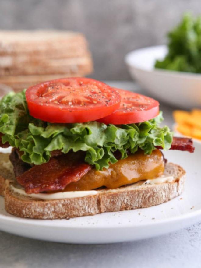 Cheeseburger με μπέικον, μαρούλι και ντομάτα, σερβιρισμένο σε φρυγανισμένο λευκό ψωμί