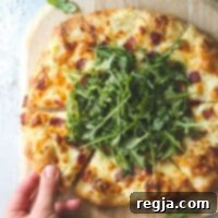 Αυτή η απλή αλλά εντελώς ακαταμάχητη λευκή πίτσα με τρία τυριά είναι καλυμμένη με τραγανό μπέικον και φρέσκια ρόκα για μέγιστη γεύση.